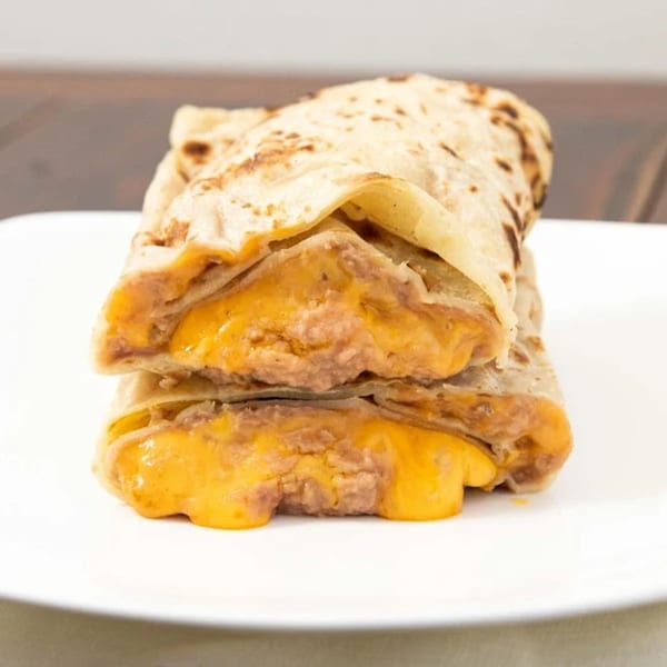Two stacked burritos from Taco Plus, filled with melted cheese and refried beans.