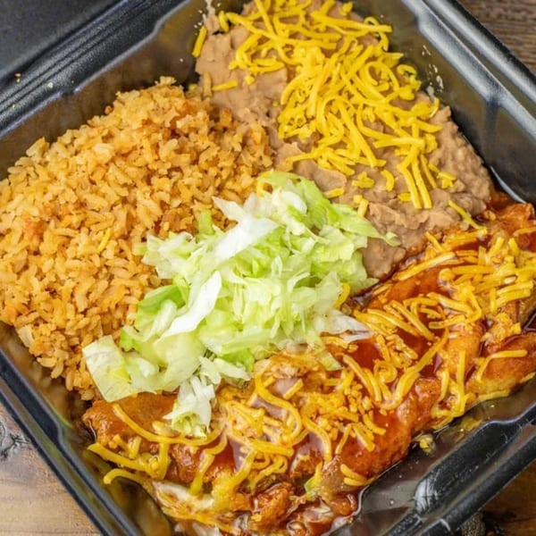 A black takeout container filled with Mexican food: rice, refried beans, and enchiladas topped with cheese and lettuce.