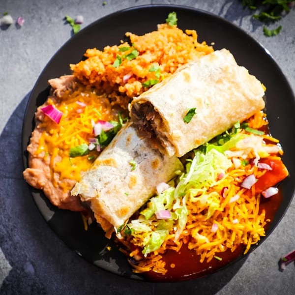 A black plate with a burrito, refried beans with cheese, and Mexican rice, from Taco Plus.